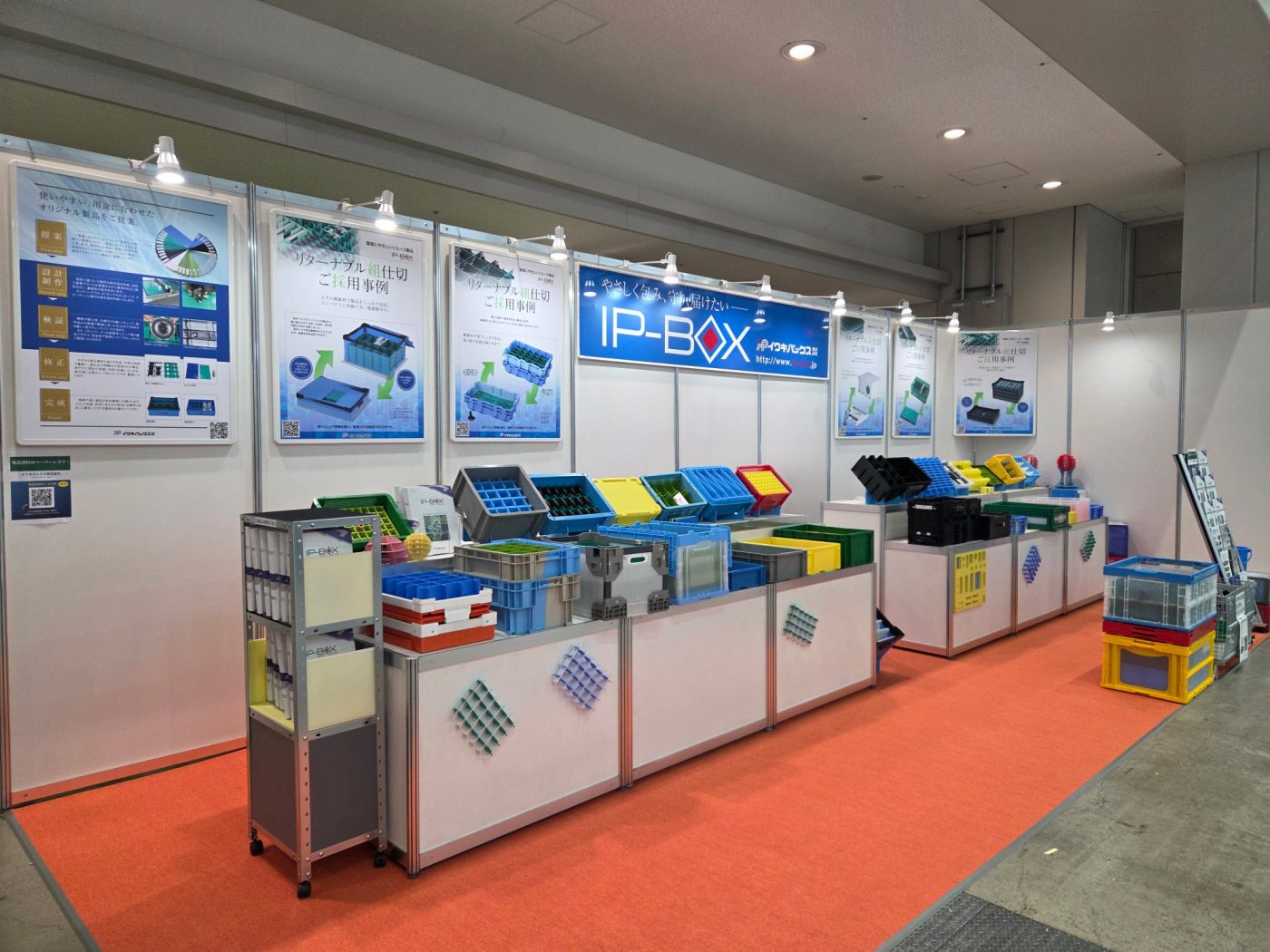IP-BOXのブース全景。壁面のパネルの前に、折りたたみコンテナと仕切りの実物が並ぶ展示台