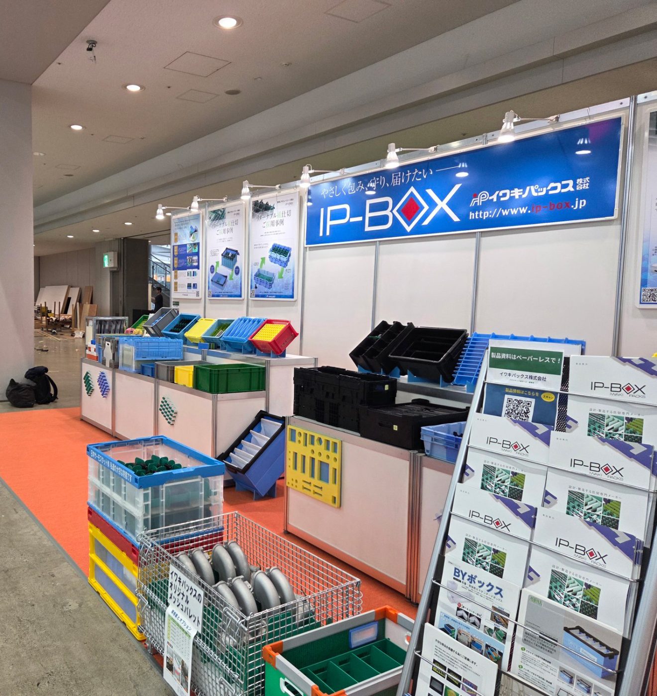 展示台に並ぶ仕切り入りのコンテナと、製品カタログを並べたスタンド